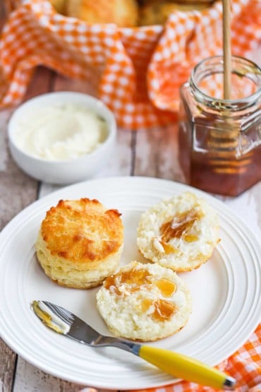 Two biscuits sitting on a white plate, one that has been split open and drizzled with honey.