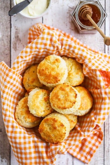 An overhead view of a basket that is lined with a kitchen cloth and is filled with homemade Southern biscuits.