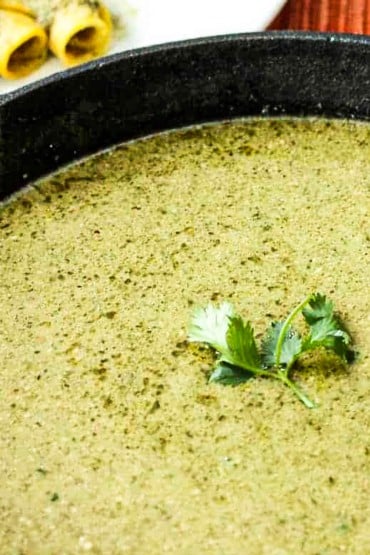 A black cast-iron skillet filled with pumpkin seed (Pipián) sauce with a sprig of cilantro in the middle.