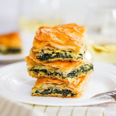 A stack of three squares of spanakopita on a white plate.