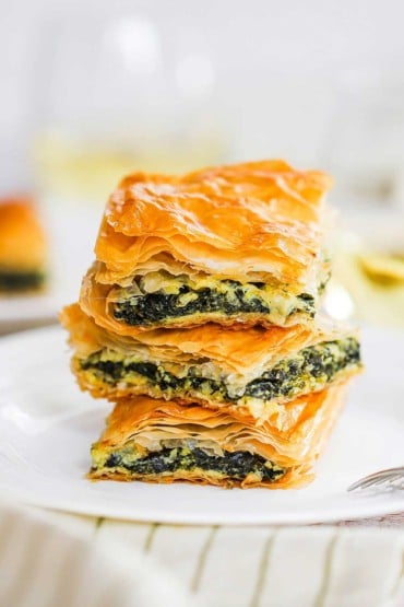 A stack of three squares of spanakopita on a white plate.