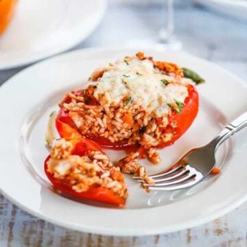 A turkey and rice stuffed bell pepper that has been cut open on a white plate sitting next to a glass of wine.