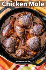 An overhead view of baked chicken mole pieces in a large black cast-iron skillet sitting next to a large wooden spoon.