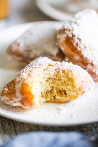 Close up of a half eaten beignet covered in powdered sugar on a white dessert plate.