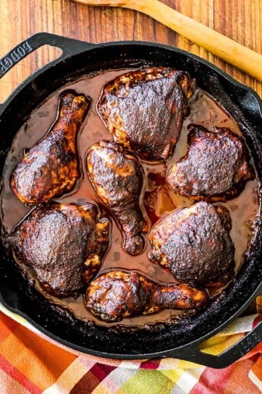 An overhead view of baked chicken mole pieces in a large black cast-iron skillet sitting next to a large wooden spoon.