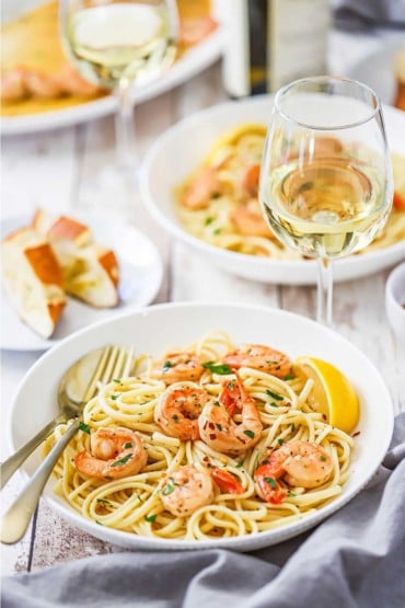 Two pasta bowls each filled with a serving of shrimp scampi both sitting next to a glass of white wine.