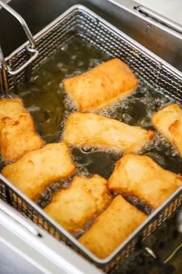 An overhead view of beignets in a deep fryer being fried.