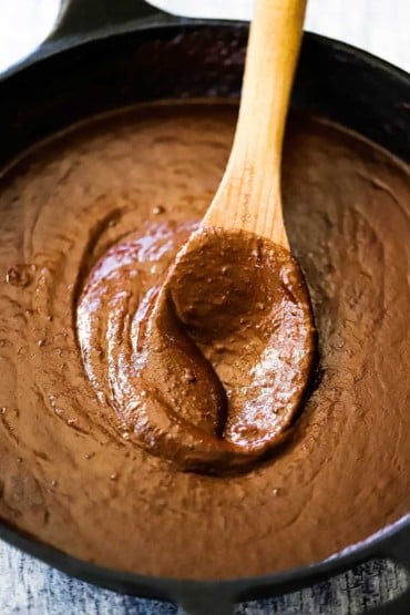 A wooden spoon inserted into the middle of a cast-iron skillet filled with mole poblano sauce.