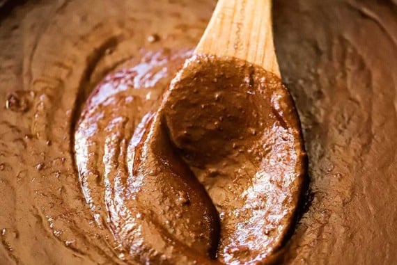 A wooden spoon inserted into the middle of a cast-iron skillet filled with mole poblano sauce.