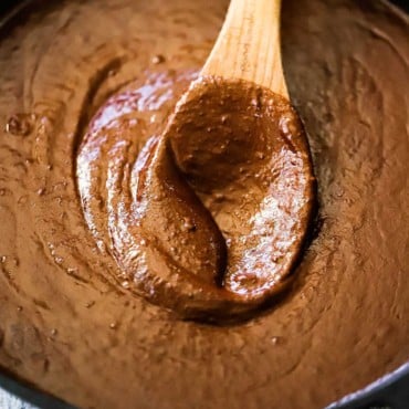 A wooden spoon inserted into the middle of a cast-iron skillet filled with mole poblano sauce.