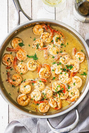 An overhead view of a large silver skillet filled with shrimp scampi in a white wine and butter sauce.