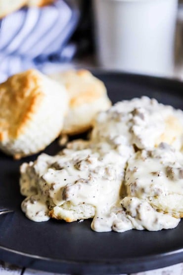 A black circular plate filled with a serving of Southern biscuits and gravy.