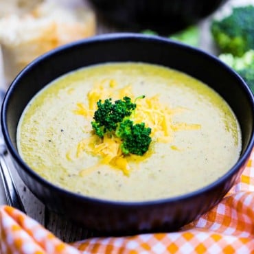 A close-up view of a black soup bowl filled with broccoli cheddar soup topped with melty shredded cheese and broccoli florets.