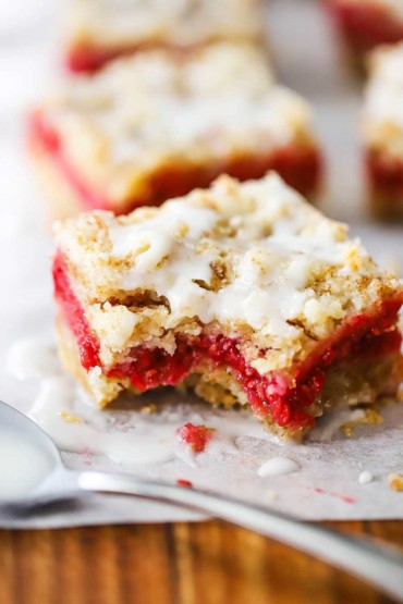 A close-up view of a raspberry Linzer bar that has a bite taken out of it and is sitting on a sheet of parchment paper.