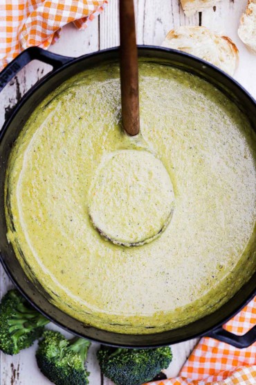An overhead view of a large black pot filled with puréed broccoli soup with a large wooden ladle in the middle of it.