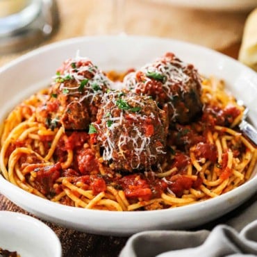 A close-up view of a white bowl filled with a serving of spaghetti and meatballs with parmesan cheese shredded over the top.