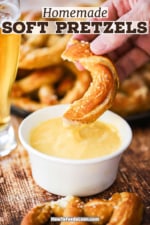 A person raising a portion of a pretzel that has been dipped into a bowl of cheese sauce.