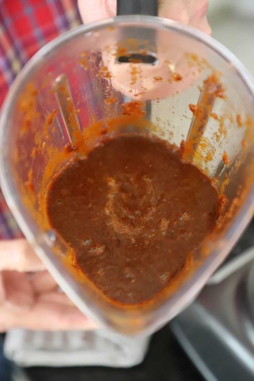 A view looking into the top of a blender that is half-full of puréed ancho chili sauce.