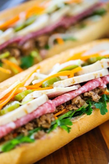 A close-up view of a banh mi sandwich stuffed with cilantro, cold cuts, sliced pork rolls, and vegetables.