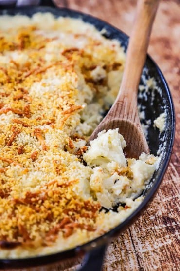 A close-up view of cauliflower gratin in a baking dish with a wooden spoon inserted into the casserole.