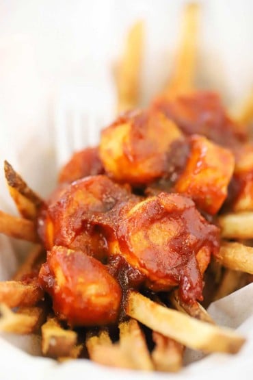 A close-up view of Germany currywurst sitting on homemade French fries in a basket lined with parchment paper.