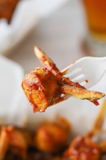 A white plastic fork holding up a bite-sized piece of cooked Bavarian bratwurst as well as a couple of French fries with a coating of curry tomato sauce on it.