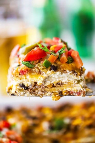 A slice of a Mexican lasagna raised up with a metal spatula.