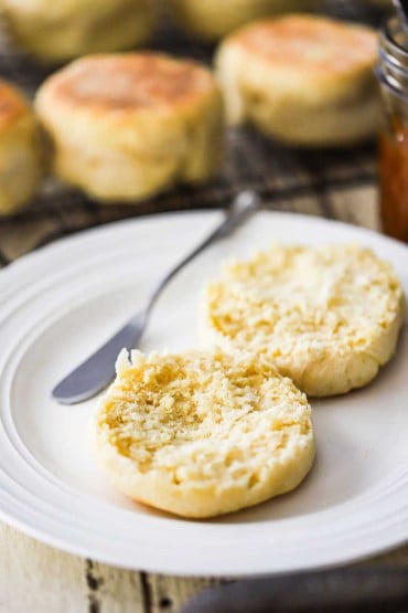 An un-toasted English muffin that has been split open and placed on a white plate next to a butter knife.