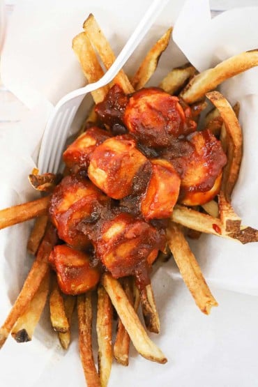 An overhead view of a small food basket filled with a layer of French fries that are topped with sliced German sausage in a currywurst sauce.