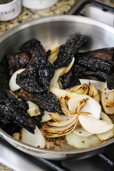 About 12 dried ancho chilis and quartered whole onions that have been toasted and roasted in a large steel skillet.