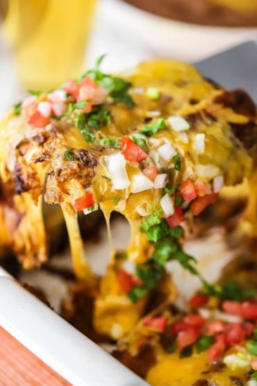 Two cheese enchiladas being raised out of a baking dish with large cheese pull from dish to the spatula.