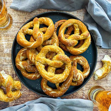 An overhead view of a circular black platter filled with a stack of homemade soft pretzels.