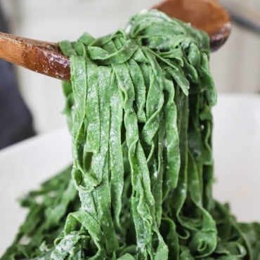 A large wooden spoons lifting up cooked fresh spinach pasta from a bowl.