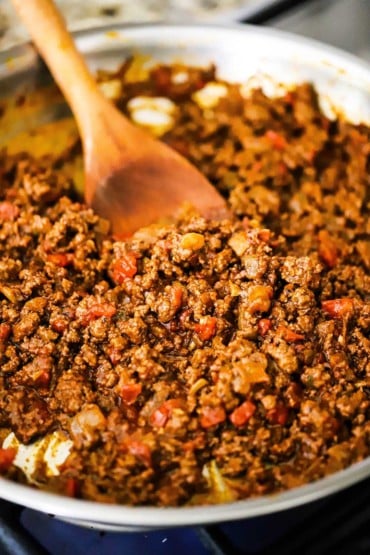 A close-up view of a large silver skillet filled with homemade ground beef taco meat with a wooden spoon inserted in it.