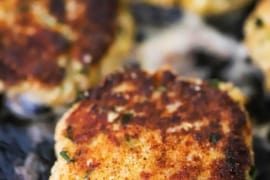 A close-up view of a Southern-style crab cake simmering on a hot cast-iron flat skillet.