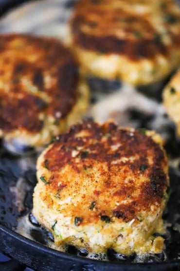 A close-up view of a Southern-style crab cake simmering on a hot cast-iron flat skillet.