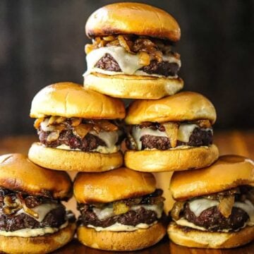 A pyramid stack of gourmet beef sliders on a wooden cutting board.