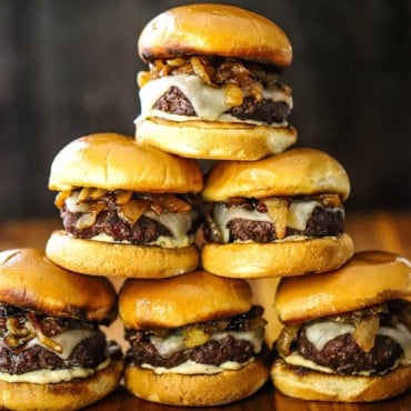 A pyramid stack of gourmet beef sliders on a wooden cutting board.