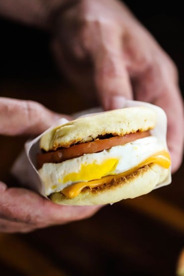 A person holding an egg mcmuffin copycat that has been wrapped in white wax paper.