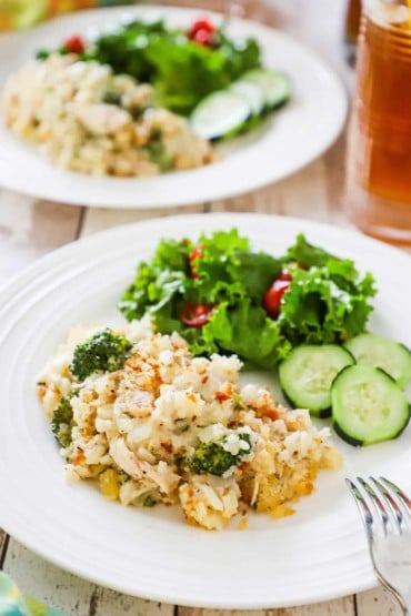 A dinner plate filled with a serving of chicken and rice casserole sitting next to a green leaf salad and several slices of cucumber.