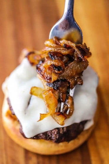 A fork being used to place caramelized onions onto a beef slider topped with melted provolone cheese.