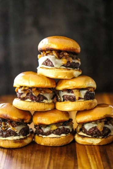 A pyramid stack of gourmet beef sliders on a wooden cutting board.