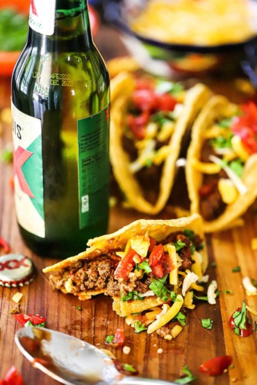 A close-up view a crispy Tex-Mex beef taco that has had a bite taken out of and set on a cutting board next to a bottle of Mexican beer.