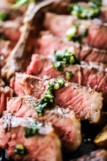 A close up view of sliced bistecca alla Fiorentina with sautéed herbs and minced garlic drizzled over the top.