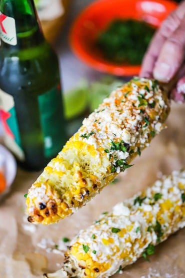 A person holding a ear of Mexican corn called elote that has a couple of bites taken out of it.