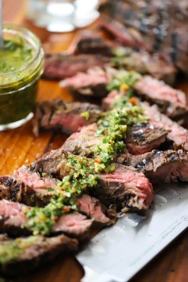 A straight-on view of sous vide skirt steak that has been cut into slices on a cutting board with a thin strip of chimichurri sauce spread across the top of the meat.