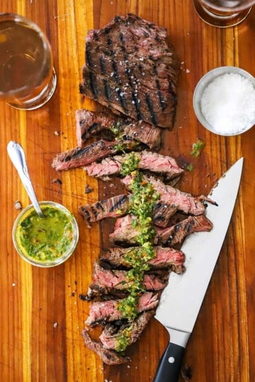 An overhead view of a sous vide skirt steak on a cutting board with half of it cut into strips and topped with homemade chimichurri sauce.