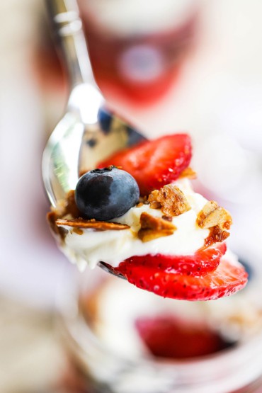 A spoon holding up a serving of fresh fruit, Mascarpone and yogurt sauce, and homemade granola.