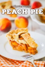 A slice of homemade peach pie sitting on a white dessert plate with whole fresh peaches sitting behind the plate.