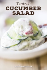 A close-up view of a wooden spoon filled with a pile of creamy tzatziki cucumber salad.